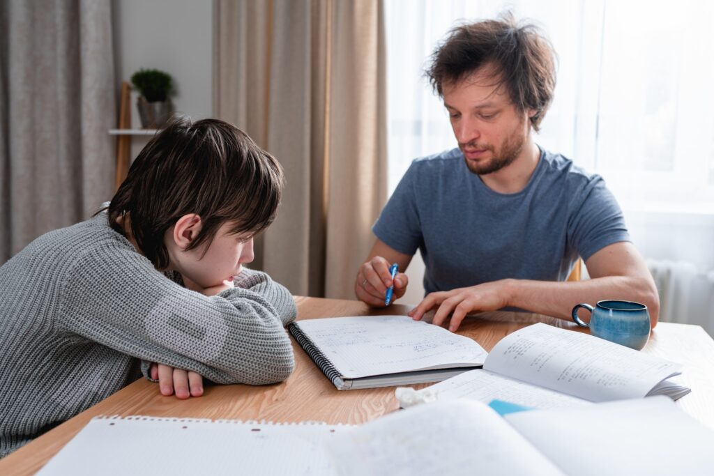 Adult man helping his son doing lessons at home during lockdown. Difficulties of home education