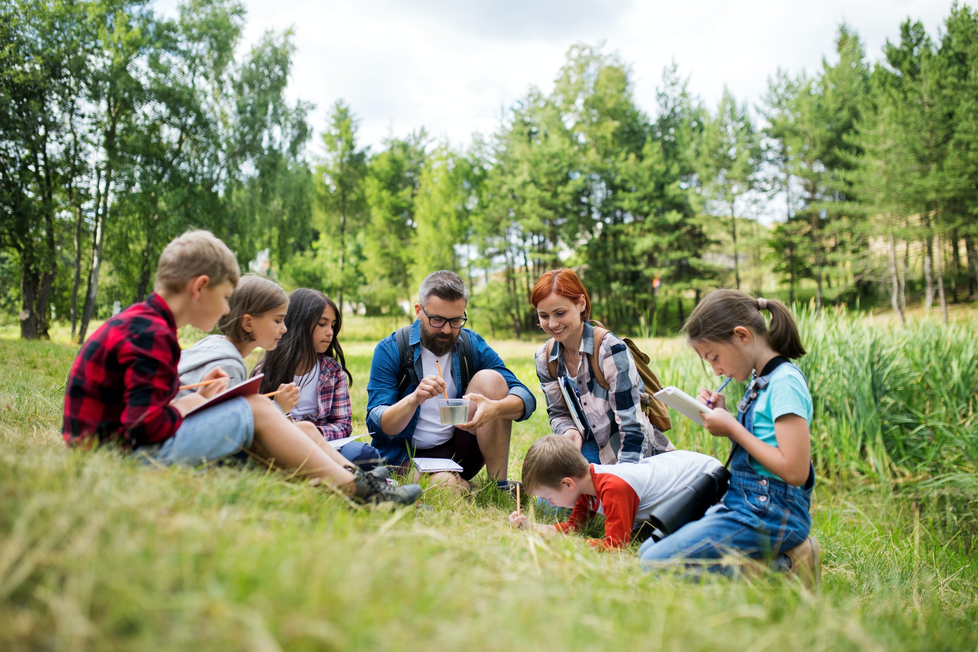 Group of school children with teacher on field trip in nature, learning science