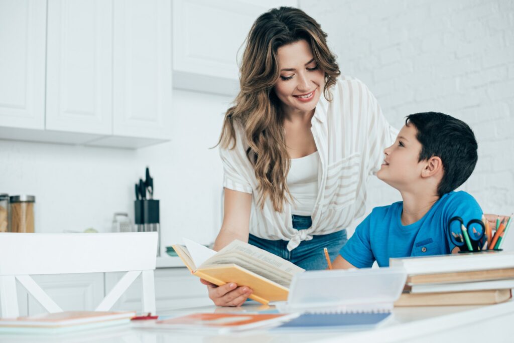 portrait of smiling mother helping son with homework in kitchen at home