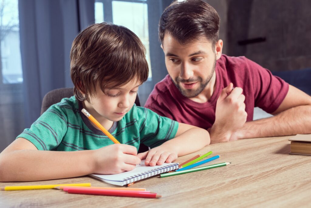 side view of father looking at concentrated son doing homework