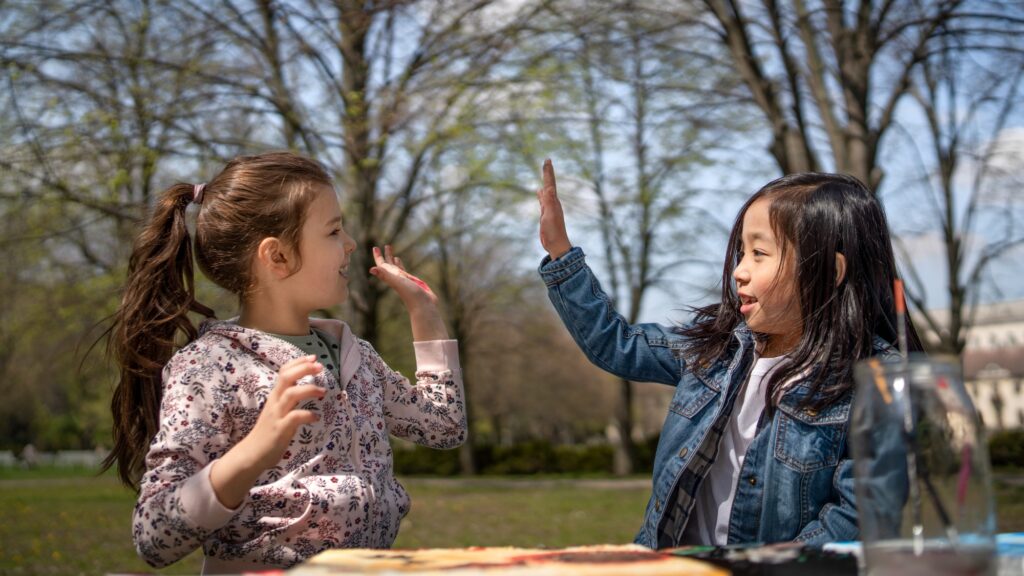 Small children painting pictures outdoors in city park, learning group education concept