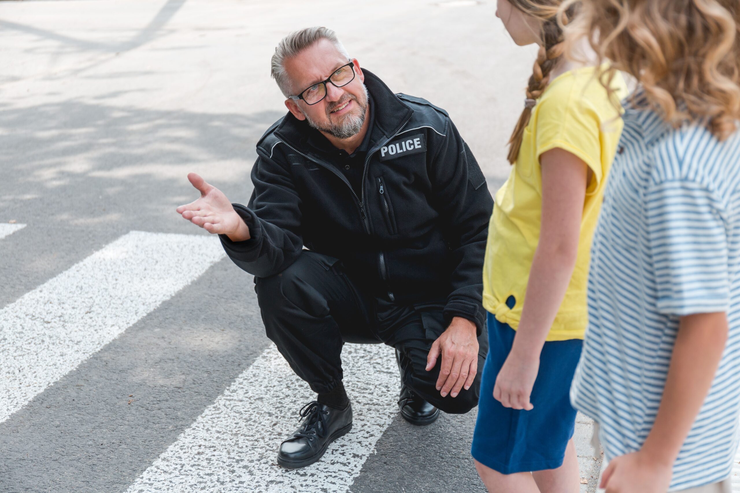 Policeman crouching in front of a pedestrian explains to a group of school children how to cross the street